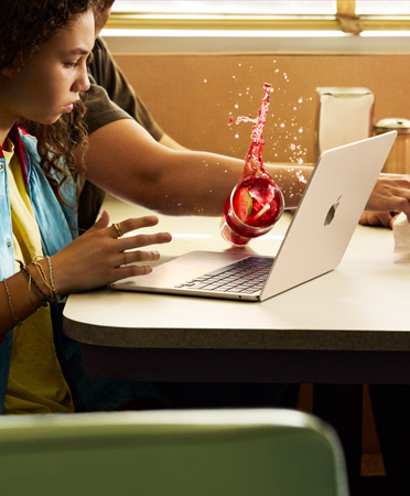 En person som sträcker sig efter något på en restaurang och spiller en kyld dryck över en öppen MacBook