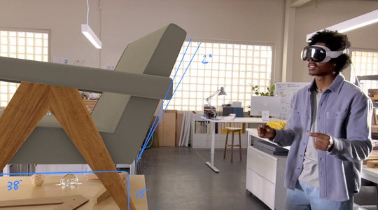 Une personne d’une équipe de conception portant un Apple Vision Pro mesure la représentation 3D d’une chaise; avec ses pouces et ses index joints, elle bouge les mains pour faire pivoter la chaise