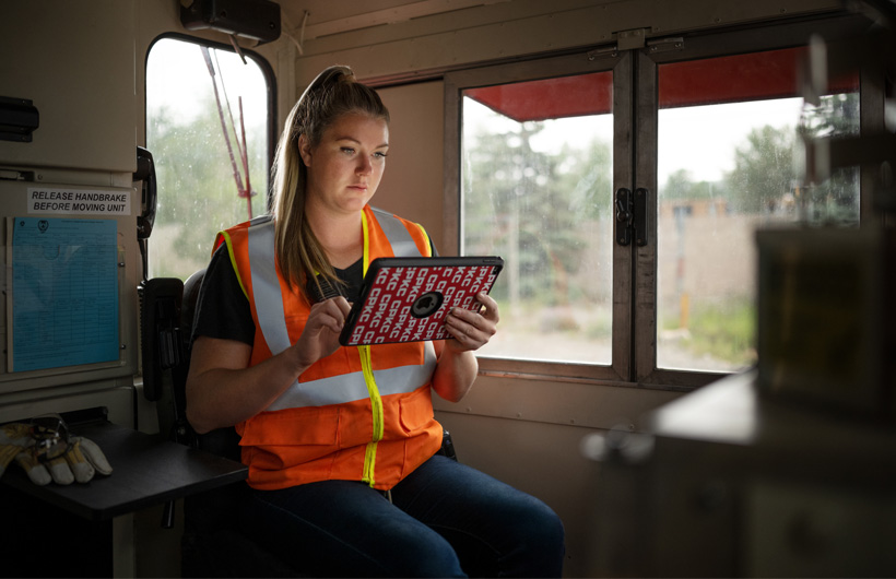 A railway worker sits inside a stationary train wagon and references an iPad