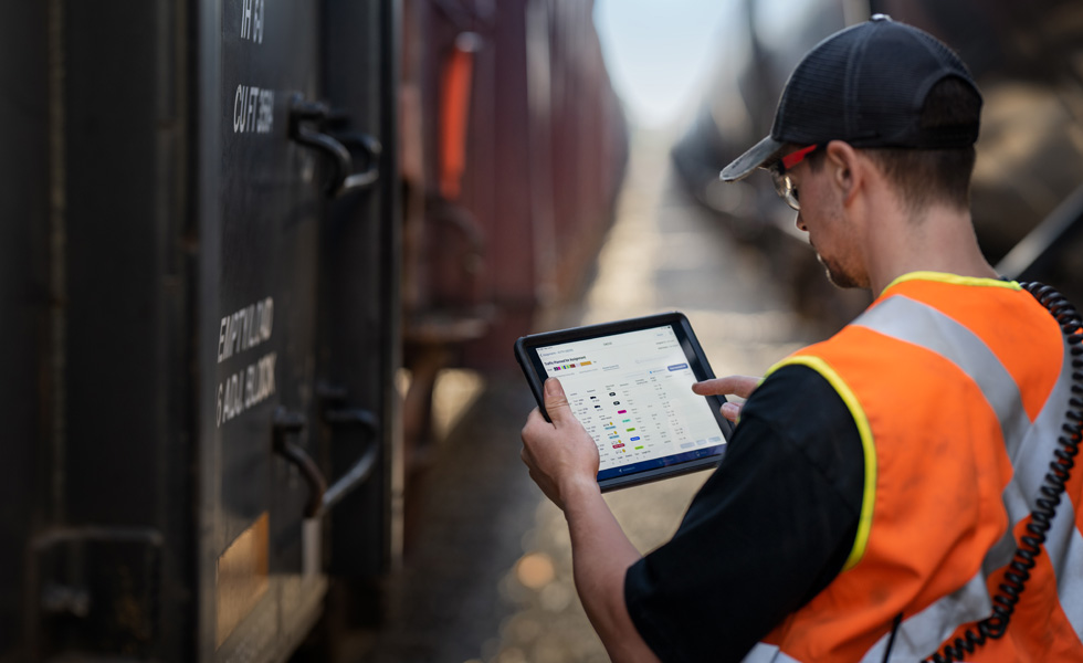 A railway worker stands beside a train checking an iPad that displays scheduling information