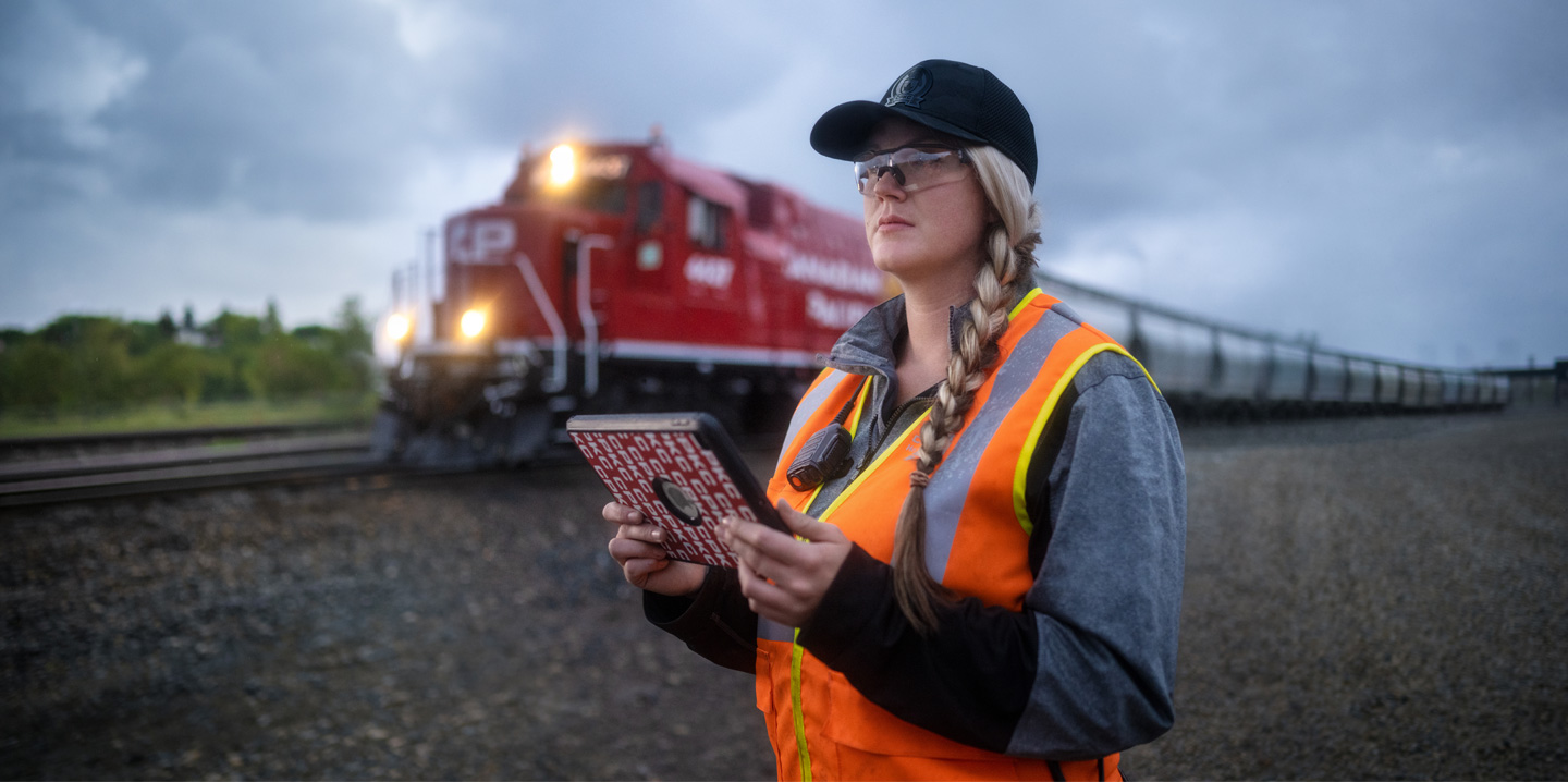 A railway worker holds an iPad and looks out at the tracks as a train passes by