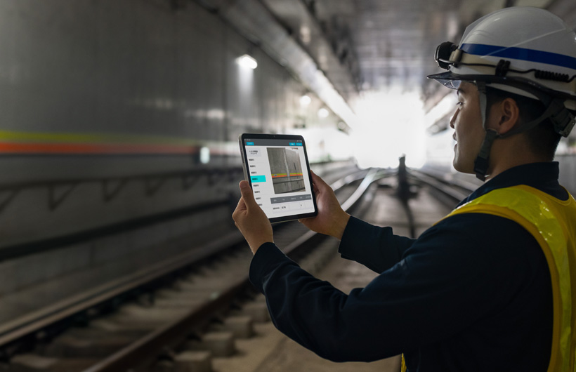 En vedlikeholdsarbeider i tunnelene til Tokyo Metro holder opp en iPad for å ta et bilde av sporene mens en kollega ser på.