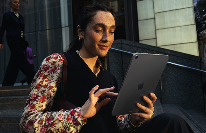 Una persona sentada en las escaleras de un gran edificio utiliza un iPad Air de 11 pulgadas en gris espacial con una conexión wifi de alta velocidad para transferir archivos