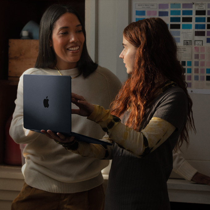 Een leerkracht en een leerling voeren een gesprek met een MacBook-laptop in de hand